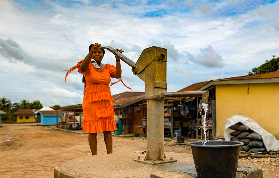 Woman in red dress pumping water at a borehole.