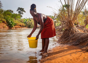 Woman collects water in yellow plastic bucket at a river.