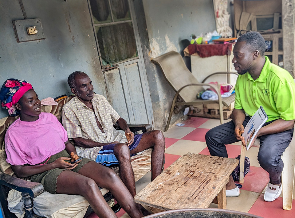 Safe Water Educator in green shirt teaching a father and daughter on porch of home.